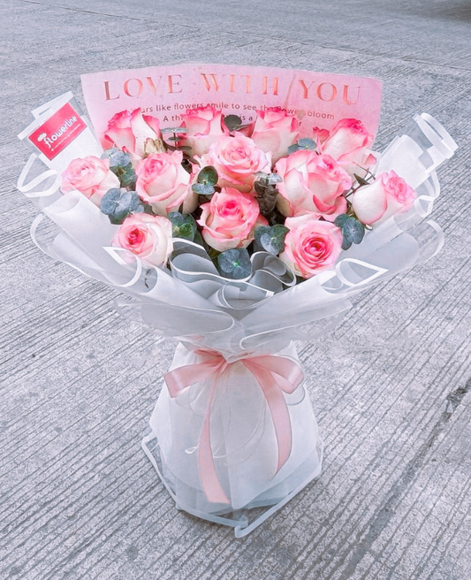 Barbara - Bouquet of two-toned pink roses with a white wrap and pink ribbon on a gray surface.